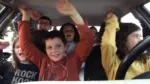 Un groupe d'enfants occupe tous les sièges de l'habitacle d'une voiture.Ils lèvent les bras en l'air et arborent des sourires radieux.