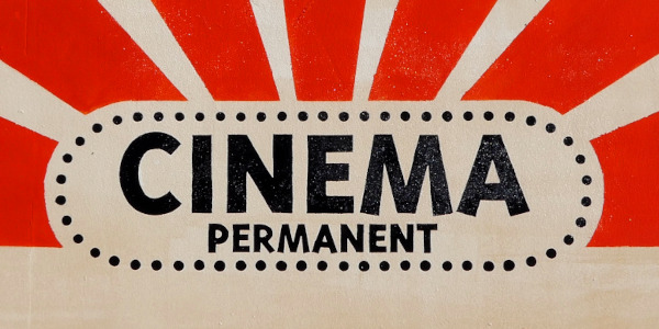 Les mots Cinéma permanent sont inscrits en noir sur un fond au motif boisé. Des pois noirs encerclent le texte et de larges rayons rouge-orange se déploient sur la moitié haute.
