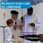 Deux prêtres et un enfant sous un parapluie, sur fond de plan d'eau. Ils sourient. L'un des prêtres est âgé et blanc, l'autre jeune et noir.