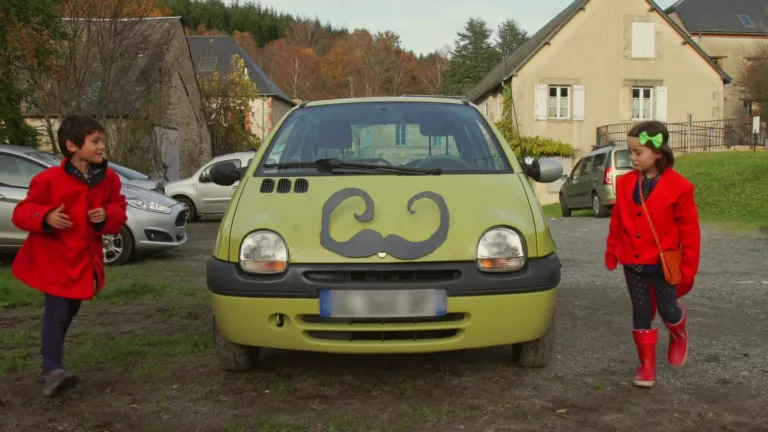 Deux enfants en uniforme rouge s'avancent au devant d'une voiture moustachue.