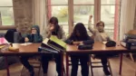 Quatre enfants sont assis dans une salle, face à des tables encombrées de classeurs et cahiers. L'un d'eux lève le doigt avec enthousiasme tandis que ses camarades sont plus ou moins avachis.